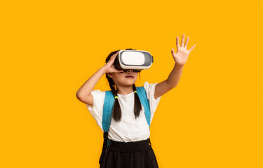 School Innovations. Asian Schoolgirl Wearing Virtual Reality Glasses Experiencing VR Standing Over Yellow Background. Studio Shot