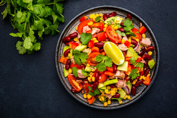 Mexican style salad with tuna, avocado, corn, beans, tomatoes and cilantro, black background, top view