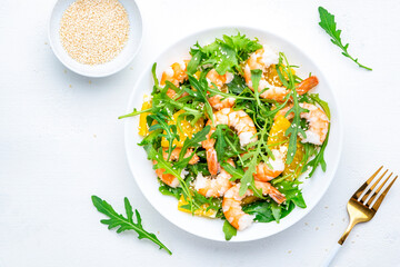 Shrimp salad with orange, arugula and sesame seeds on white background. Top view