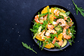 Yummy shrimp salad with avocado, orange, arugula and sesame seeds on black table background. Top view
