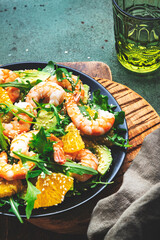 Delicious shrimp salad with avocado, orange, arugula and sesame seeds on green table background. Top view