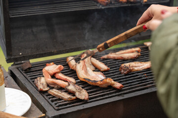 Close-up of a person handling tongs to grill bacon slices on a barbecue, capturing the sizzle, smoky flavors, and the joy of outdoor cooking, showcasing the art of grilling