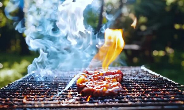 Juicy meat grilling on outdoor barbecue with flames and smoke 