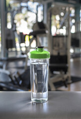 Transparent shaker bottle on a gym floor, filled with a fitness drink, surrounded by exercise equipment, symbolizing hydration and energy during a workout session.