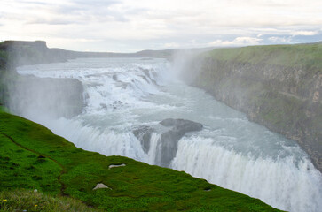 Gullfoss Waterfall, part of Iceland's golden circle route shimmers in deep blue as the icy water plunges into the gorge under dramatic skies 