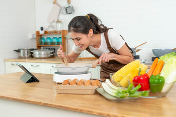 Asian Woman Cooking in Modern Kitchen Using Tablet for Recipe, Surrounded by Fresh Vegetables and Ingredients - Concept of Healthy Eating, Online Learning, and Home Cooking Lifestyle