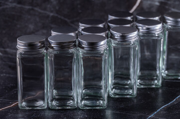 Glass empty jars with metal lids for cosmetics, spa, spices and other products on blurred dark abstract background.