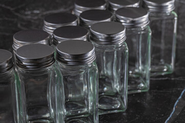 Glass empty jars with metal lids for cosmetics, spa, spices and other products on blurred dark abstract background.