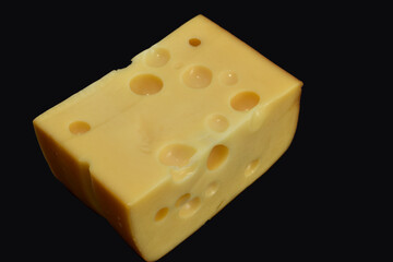 Hard Maasdam cheese with large holes lies on a dark background.