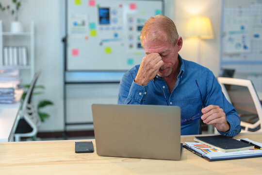 Stressed mature entrepreneur experiencing migraine and eye strain after using computer for a long time, suffering from blurry vision and holding eyeglasses in hand