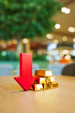 Gold bars and red arrow pointing down placed on the table, concept of gold price is decreasing due to going up high.