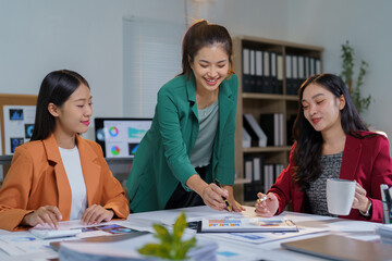Fototapeta premium Three asian businesswomen are discussing financial charts and analyzing statistical graphs while working together in modern office, showing teamwork and cooperation