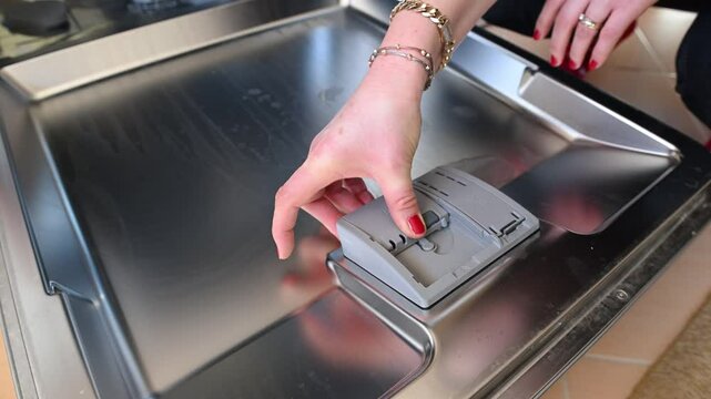 A woman's hand filling the detergent container of a dishwasher.
