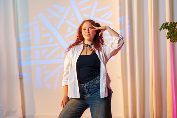 Fototapeta premium A young woman with curly red hair poses in front of a patterned background