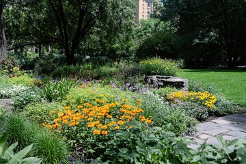 Obraz premium Vibrant Flower Garden with Lush Greenery in City Park on a Sunny Day