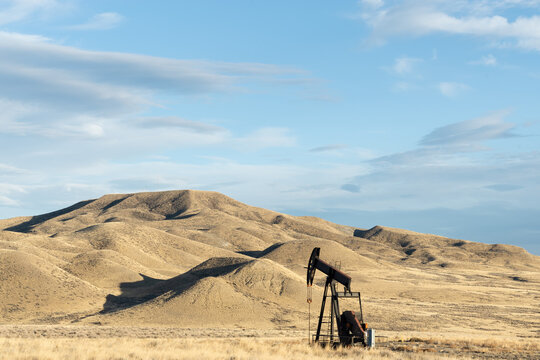 Single working oil rig in a plains area of Texas Oklahoma New Mexico or North Dakota in the unpopulated countryside pumping for production of fossil fuel with rolling hills in the distance