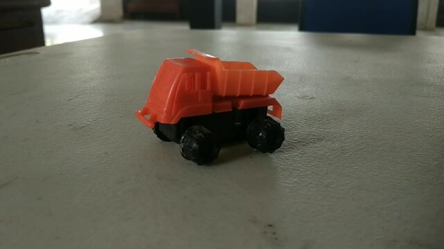 A small orange and black toy dump truck on a light-colored surface. Simple childhood plaything.