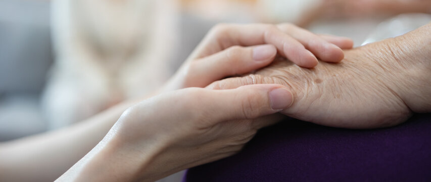 A younger hand tenderly holds an elderly one, symbolizing the loving bond between a mother and child. Mother's day concept.
