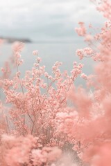 Naklejka premium Delicate pink flowers create a dreamy foreground against a blurred seascape, capturing the serene beauty of nature, vertical