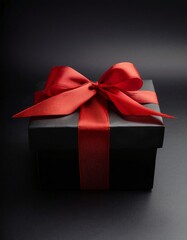 Obraz premium A black gift box adorned with a red ribbon against a black background features a red bow atop it