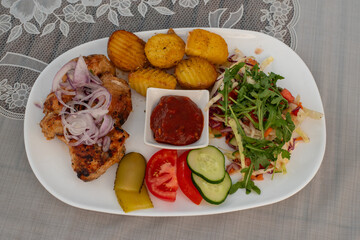 Top view of grilled chicken with tomato sauce, baked potatoes and fresh vegetables on the white plate. Healthy lunch.
