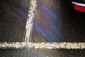 Fuel or oil stain on wet parking lot asphalt, indicated by a white line. © AleksFil