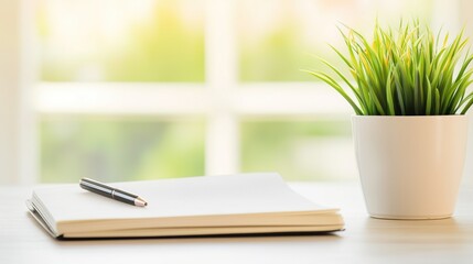 Naklejka premium Notebook and pen on desk beside green plant in bright home office setting