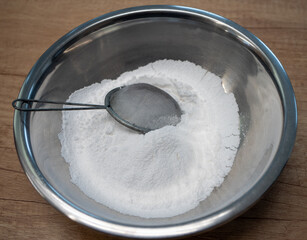 Sifted white powdered sugar in a stainless steel bowl prepared as an ingredient for baking cakes,...