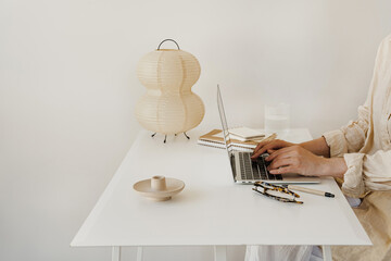 Person Typing on Laptop at Cozy Home Office Desk with Notebooks and Decorative Lamp