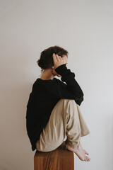 Woman wearing beige pants, black sweater sitting on wooden block. Minimalist and calm setting,...