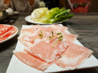 Delicious hot pot eating at a restaurant, Chinese and Japanese hot soup beef meat and pork sliced in plate, cabbage vegetable in white bowl, traditional food stock photo