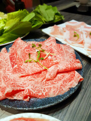 Delicious hot pot eating at a restaurant, Chinese and Japanese hot soup beef meat and pork sliced in plate, cabbage vegetable in white bowl, traditional food stock photo