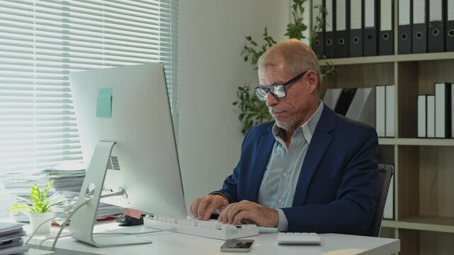 Office worker starting his workday, typing on the computer keyboard, looking at the screen, and then relaxing on his chair with his hands behind his head