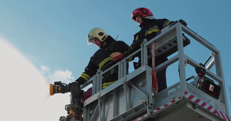 Firefighters stand in a special lifting cradle and put out a fire with a fire hose. The footage shows hard work in extreme conditions. Ideal for themes about rescue operations.