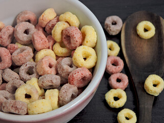 A bowl of colorful cereal with fruit flavors on top on a dark table, the focus of the color and texture of the cereal is tempting. Perfect for a healthy breakfast or snack concept.