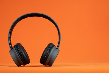 A stylish pair of black headphones showcased on a vibrant orange background