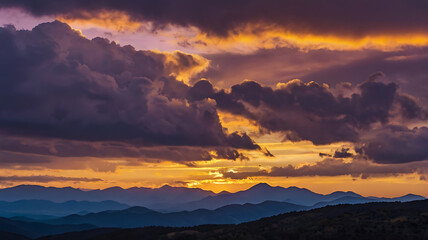 Obraz premium A vivid sunset over a mountain range, with the peaks silhouetted against a sky painted in purples, blues, and golden yellows.