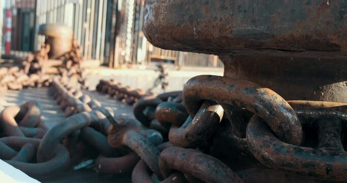 Large rusty ship chains and metal lashing blocks seen from a detailed angle. This shot highlights the durability of industrial equipment and the effects of time.