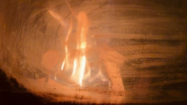 primo piano schermo intero di fuoco di legna che arde nel braciere di una vecchia stufa visto attraverso un vetro fulignoso e sporco