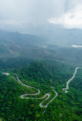 Aerial drone view of winding mountain road surrounded with greenery rainforest at Wang Kelian, Perlis, Malaysia.
