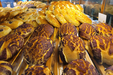 A close-up view of assorted freshly baked bread and buns displayed in a bakery, showcasing a variety of textures and toppings.