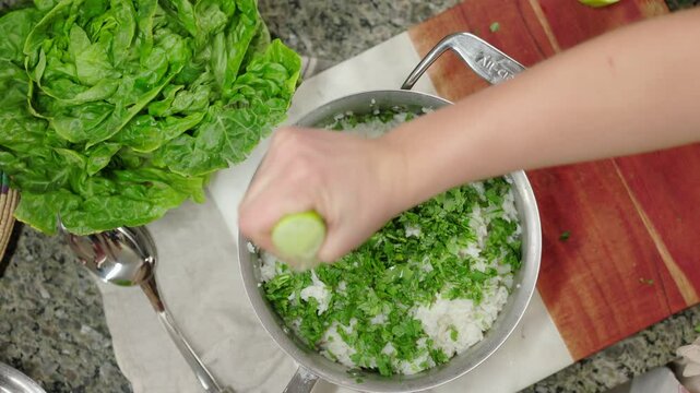 A hand squeezing lime juice over fresh cilantro and rice for a cooking process