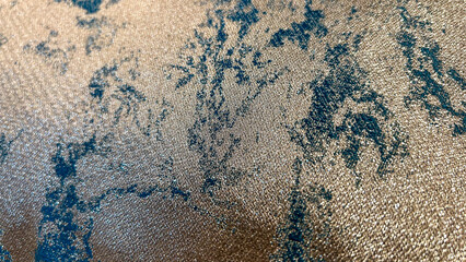 Close-up of a luxurious textured fabric with shimmering gold and teal patterns, showcasing intricate details and a refined aesthetic. Perfect for highlighting elegance and premium textile design.