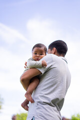 Father holding baby daughter in his arms outdoors on sunny day