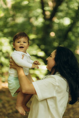 A mother walks with her son and holds him in her arms in a summer park