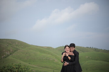 Loving young Indian couple in trendy clothes embracing against green mountains under sky on sunny day