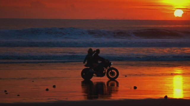 Man, woman ride vintage motorcycle or motorbike along ocean coast in Bali. Couple sits and riding on a scooter on sandy sea beach, sunset. Travelers enjoy journey on bike, love on adventure, road trip