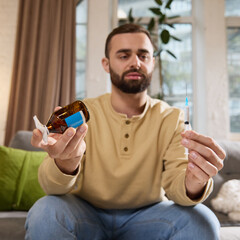 Man sitting on sofa and shows syringe filled with drug and sponge for disinfection. Routine...