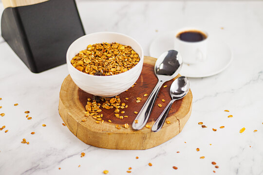 Tigela com granola, colher e caf&eacute; expresso sobre uma superf&iacute;cie de madeira, em cima de uma bancada de porcelanato branco com veios cinza Bowl of granola, spoon, and espresso coffee on a wooden surface