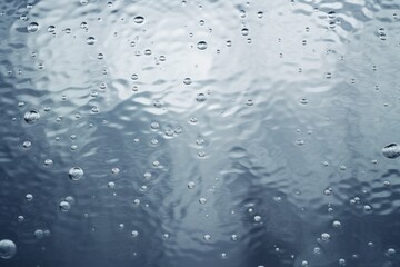 Raindrops create ripples on a calm surface reflecting soft light in a tranquil setting